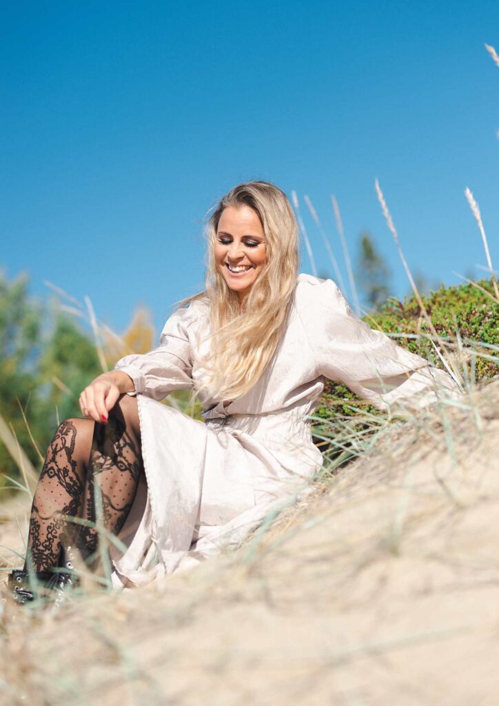 Lisa Mikovsky sitter p&aring; en sandstrand med bl&aring; himmel i bakggrunden. 