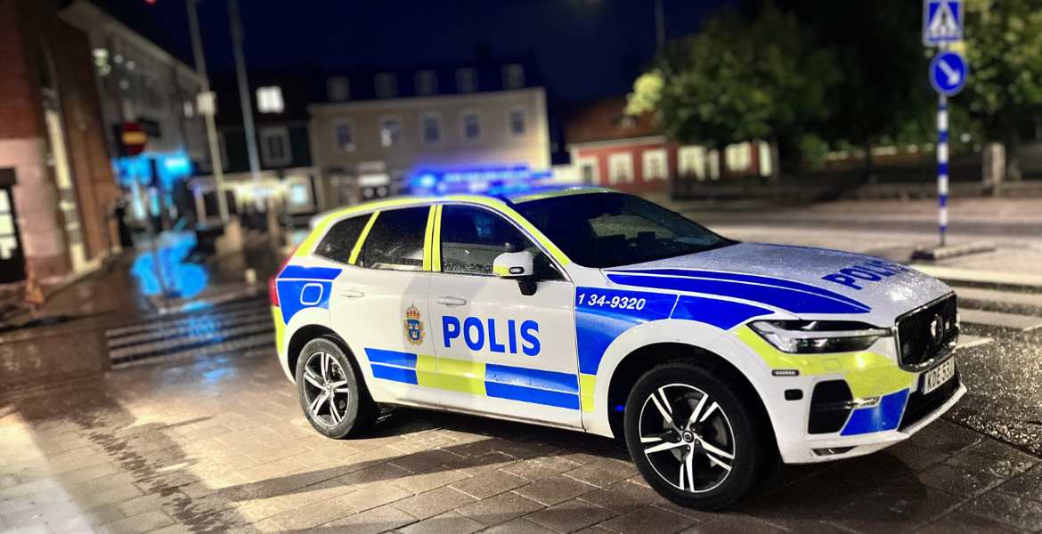 En stillastående polisbil i kvällsmörker med blåljus igångsatta.