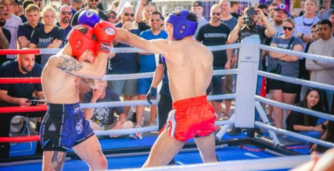 Två thaiboxare, i en ring, som slåss. Åskådare hejar på.